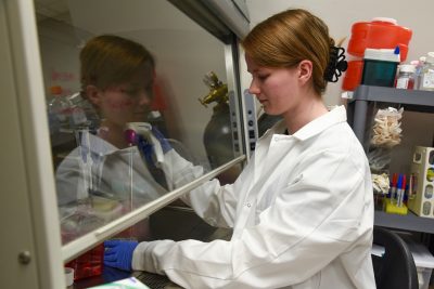 Person in a white coat doing an experiment behind glass.