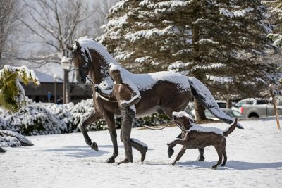 Statue of a person walking with a horse and a dog.