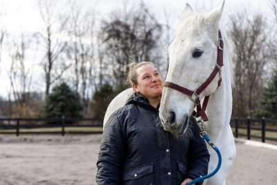 White horse and the horse's owner stand in an outdoor riding arena.