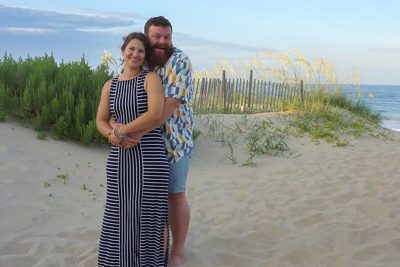 Two people posing on a sandy beach.