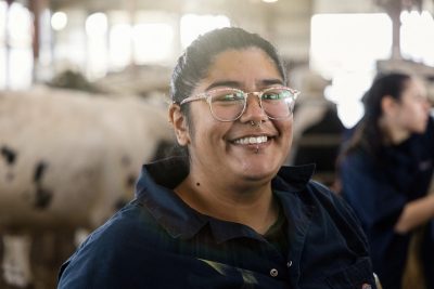 Person in blue coveralls standing in a cow barn.