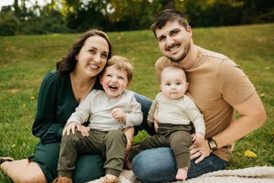 Family of four sitting on a blanket and smiling at the camera.