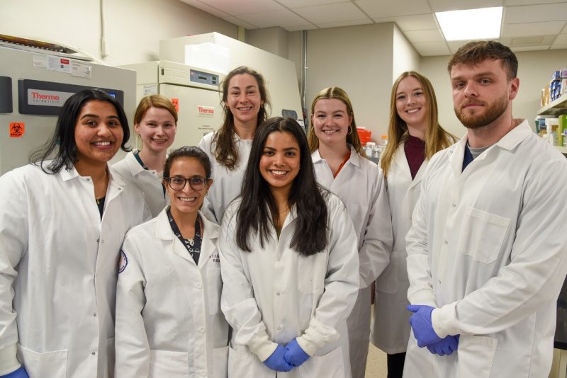 Research team standing in the lab, all wearing white coats.